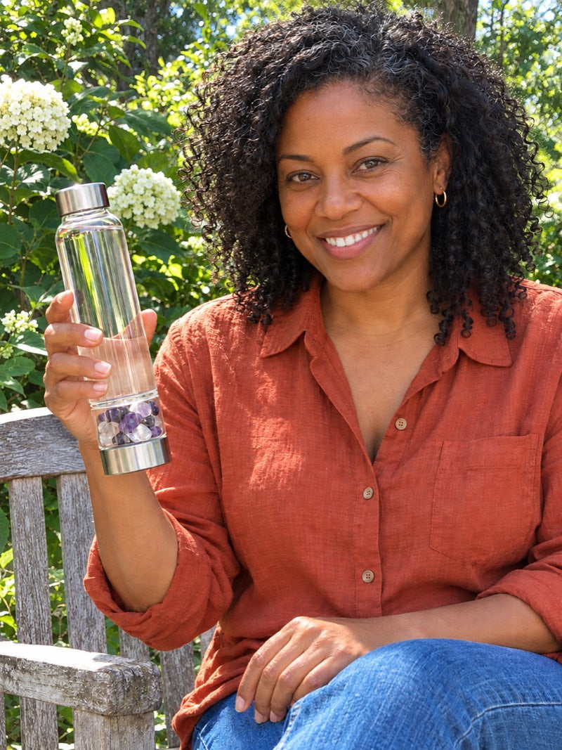 Smiling on a garden bench, holding an Elixir2Go with Amethyst and Clear Quartz